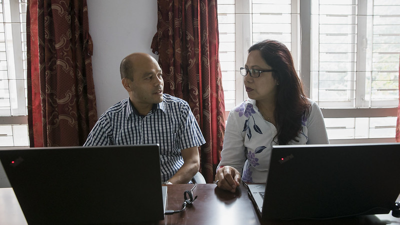 A man and a woman sitting at a table with laptops and having a conversation