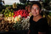 A woman standing next to her produce table and smiling