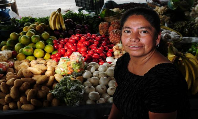 A woman standing next to her produce table and smiling